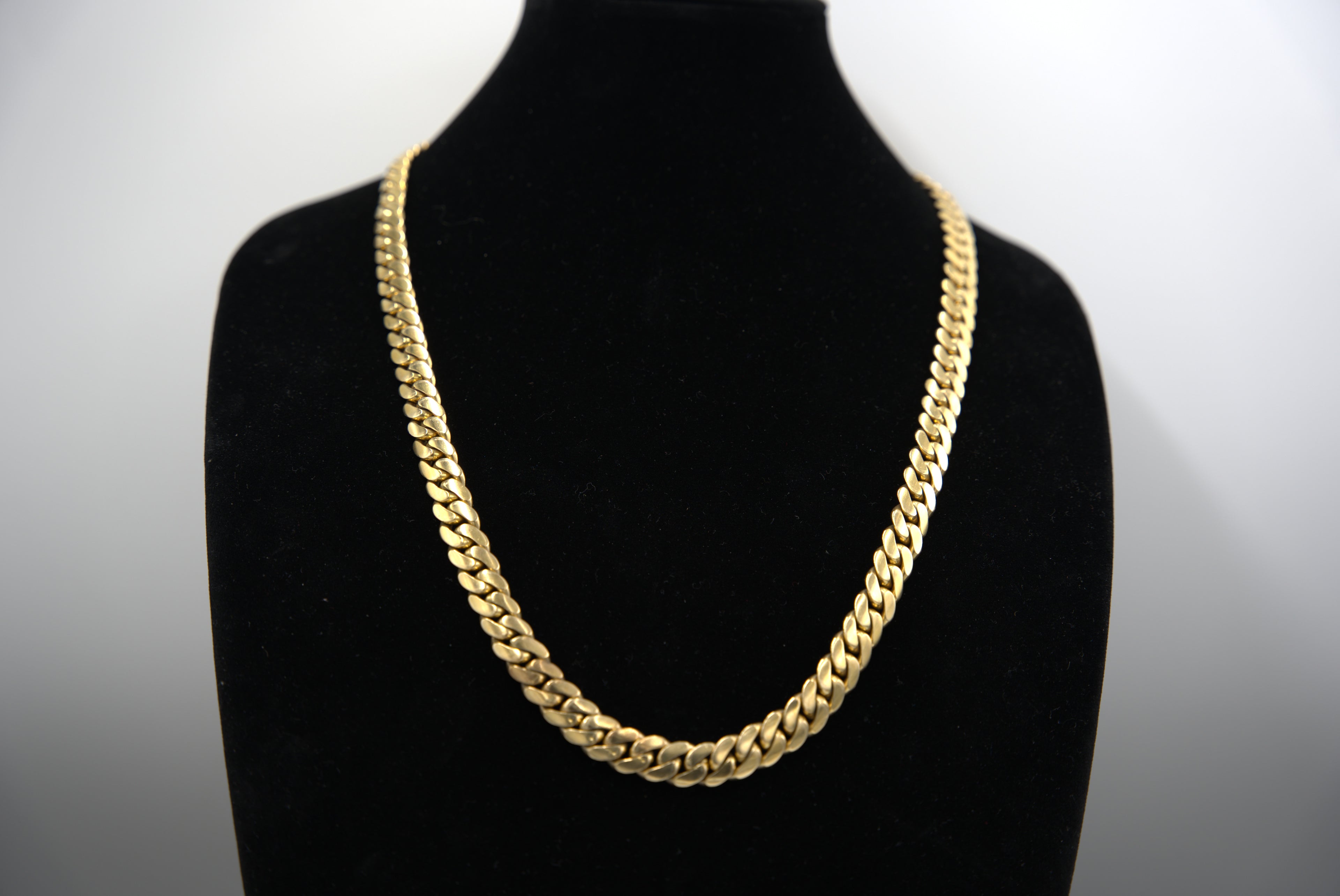 Gold chain necklace on a black mannequin against a white background