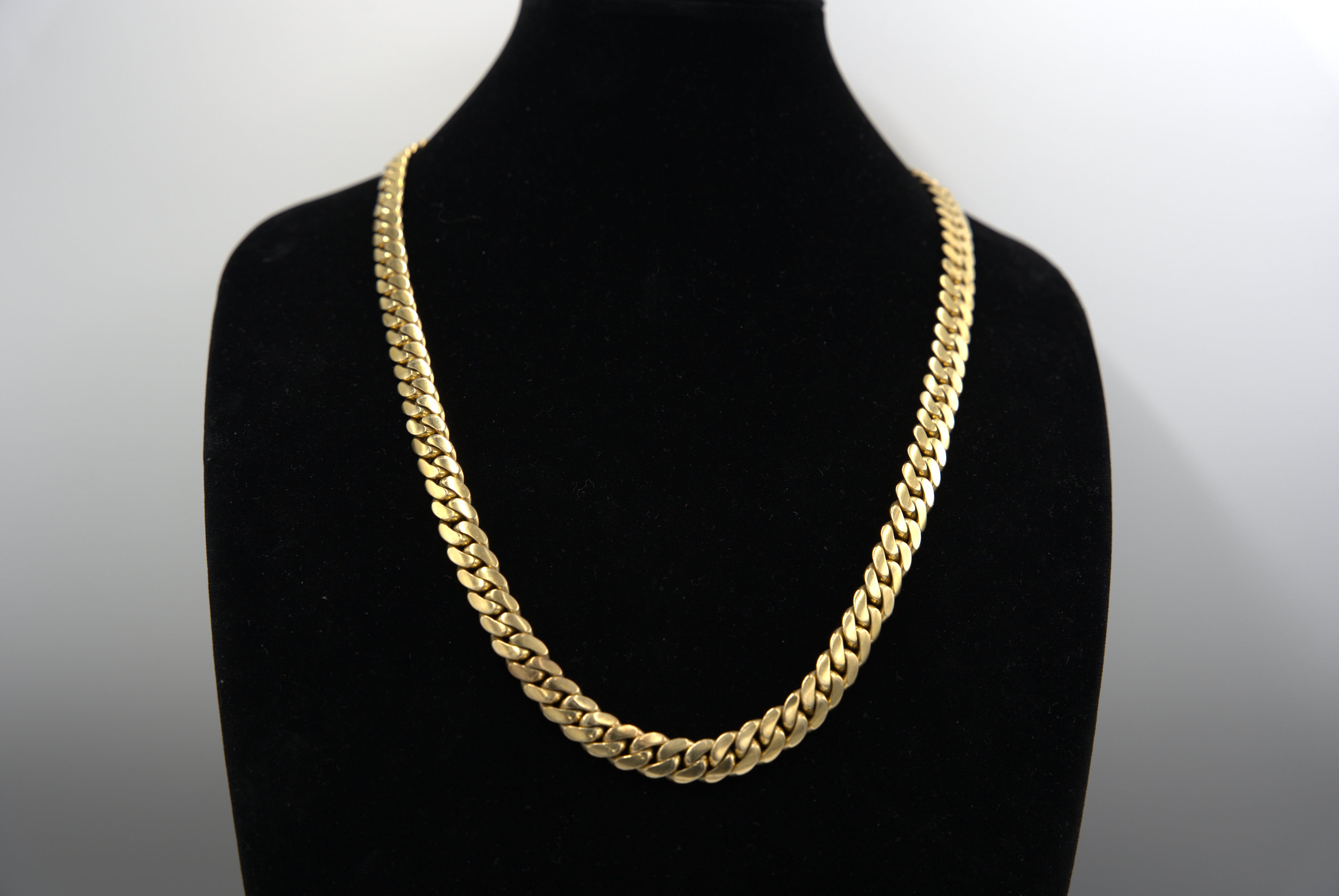 Gold chain necklace on a black mannequin bust against a white background